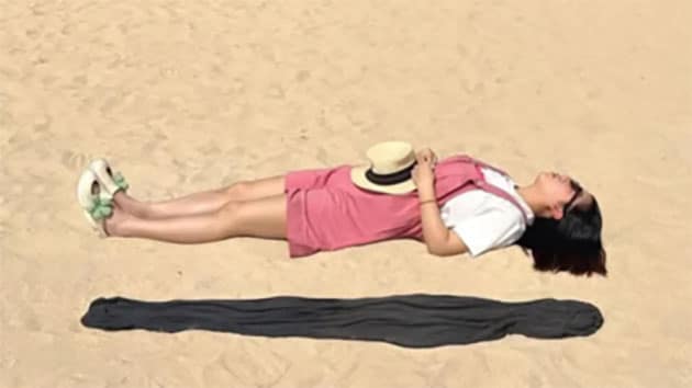 Hier schwebt in Wirklichkeit niemand. Die Frau liegt lediglich neben einem dunklen Badetuch im Sand.